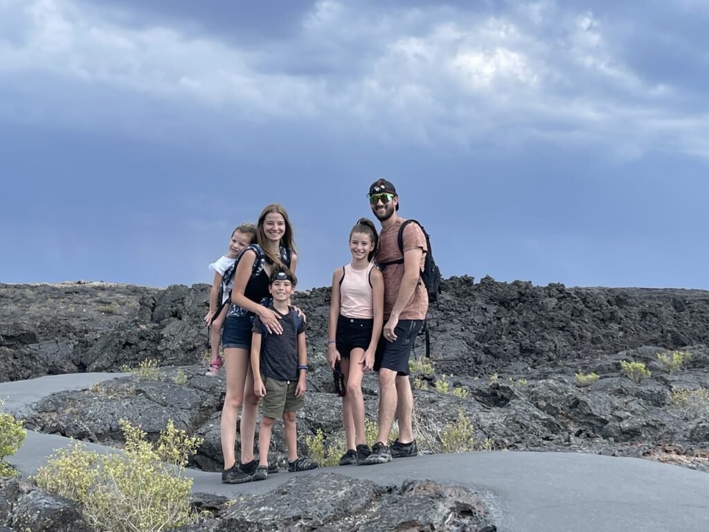 Family of 5 standing on the path to the caves at the national park in idaho, surrounded by volcanic rock and a blue sky